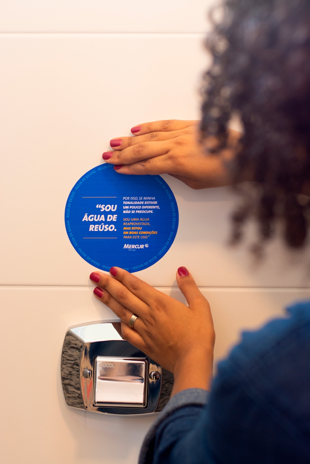 Mão de pessoa colando um adesivo escrito 'Sou agua de reuso' na parede